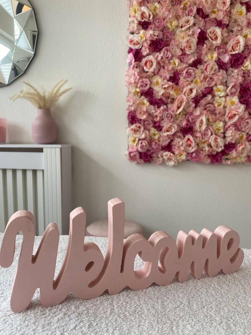 a pink wooden name sign with flowers on the wall